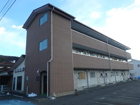 駐車場が付いた茶色い壁で3階建てのレジデンスサコウ3の写真