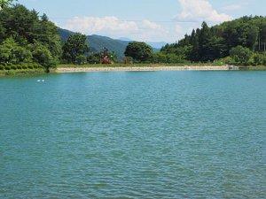 奥に青空と山が広がっているため池の写真