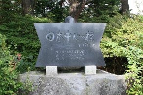 森林を背景に日本中心の標を示した石碑の写真