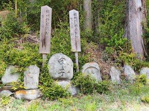 山の斜面を背景に位置する沢底仲組の道祖神の写真