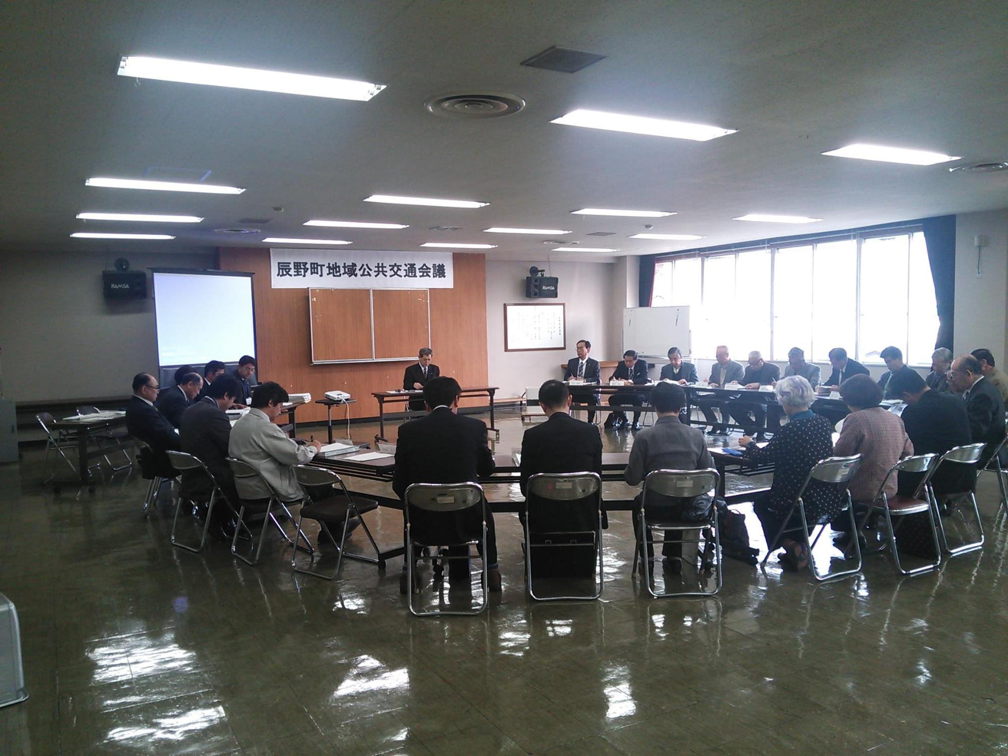 辰野町地域公共交通会議の垂れ幕が下がった部屋でたくさんの人がテーブルを囲っている写真