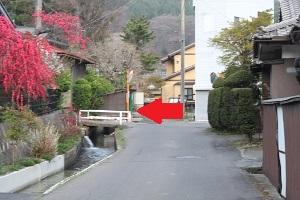 左に流れる小さな川にかかった白い橋のほうを向いた赤い矢印が描かれた写真