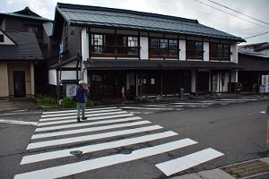 古い2階建ての家屋の前の横断歩道を人が歩いている写真