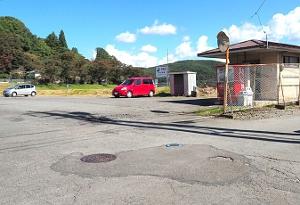 赤い車が止まっていて右手に小屋と自動販売機がある駐車場のような場所の写真